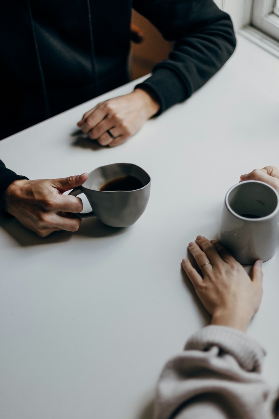Zwei Menschen mit Kaffeetassen an einem hellen Tisch